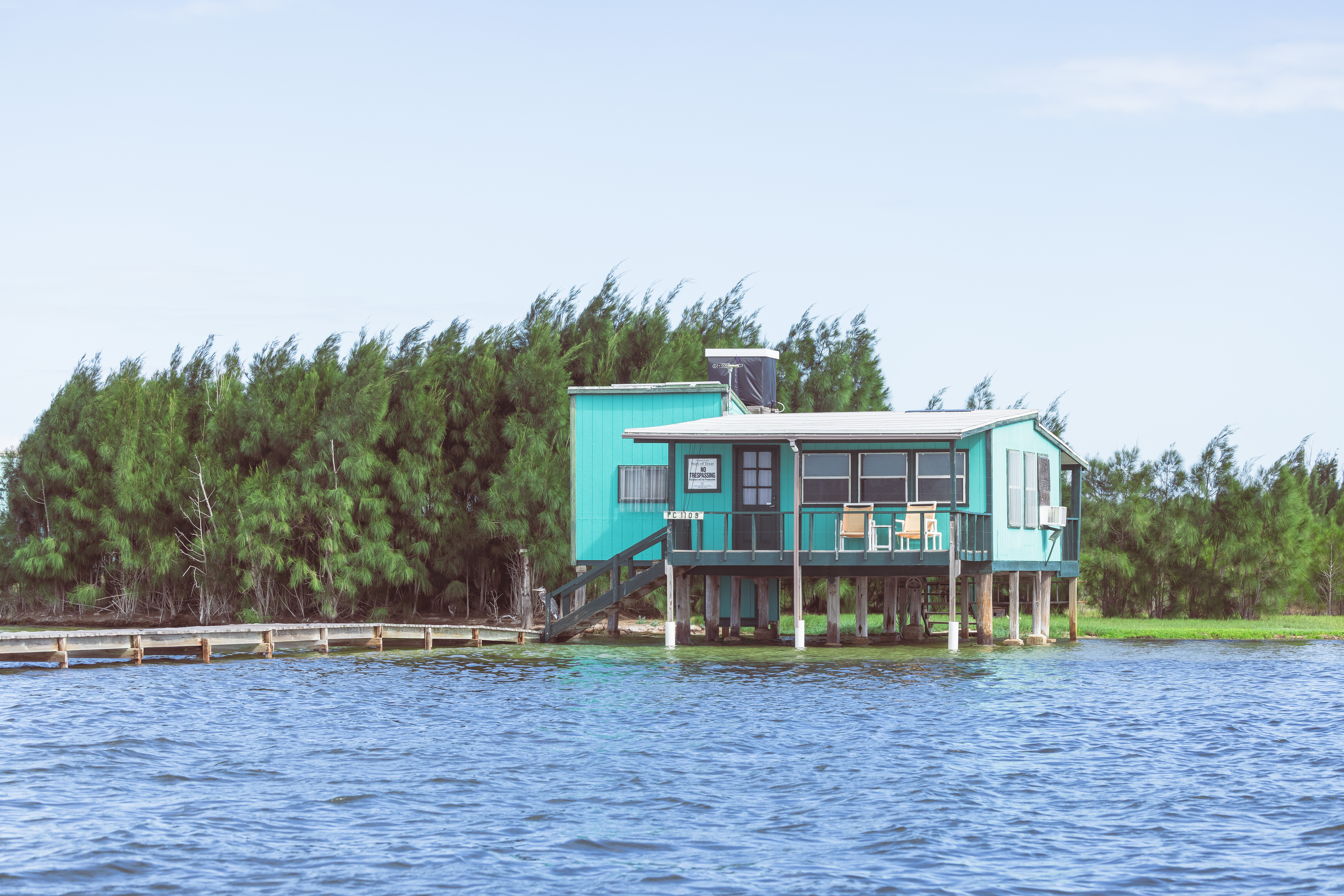 An aqua blue house sits on stilts on the shallow edge of the Laguna Madre.